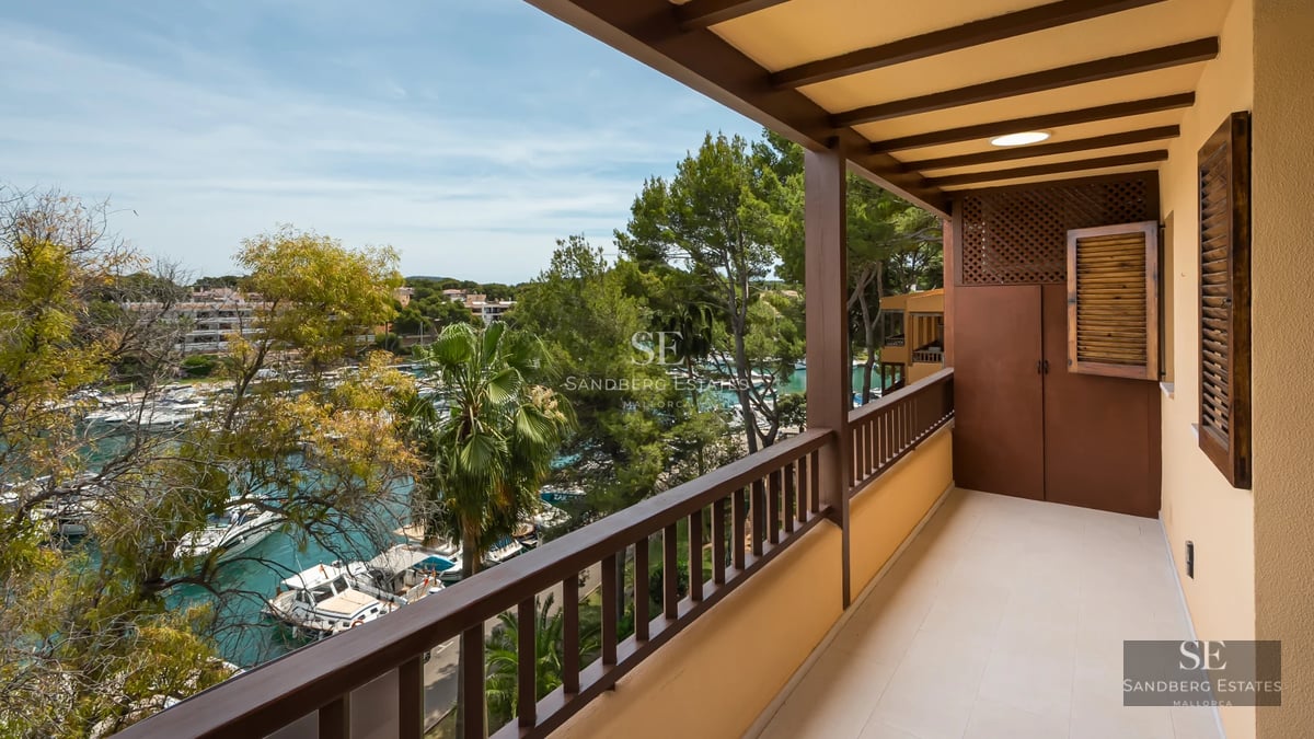 View of an infinity pool with turquoise water, bordered by light tiles. A modern house with large windows in the background.