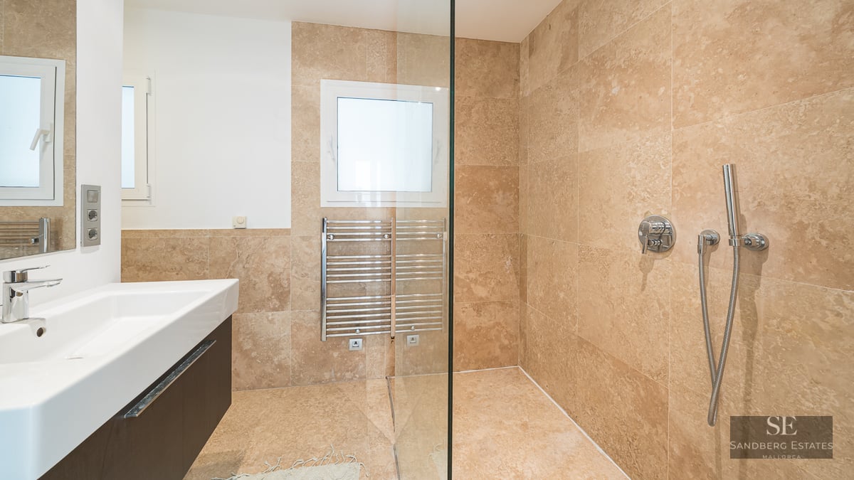 Modern bathroom featuring beige travertine tiles, a glass walk-in shower, a heated towel rack, and a white vanity sink.