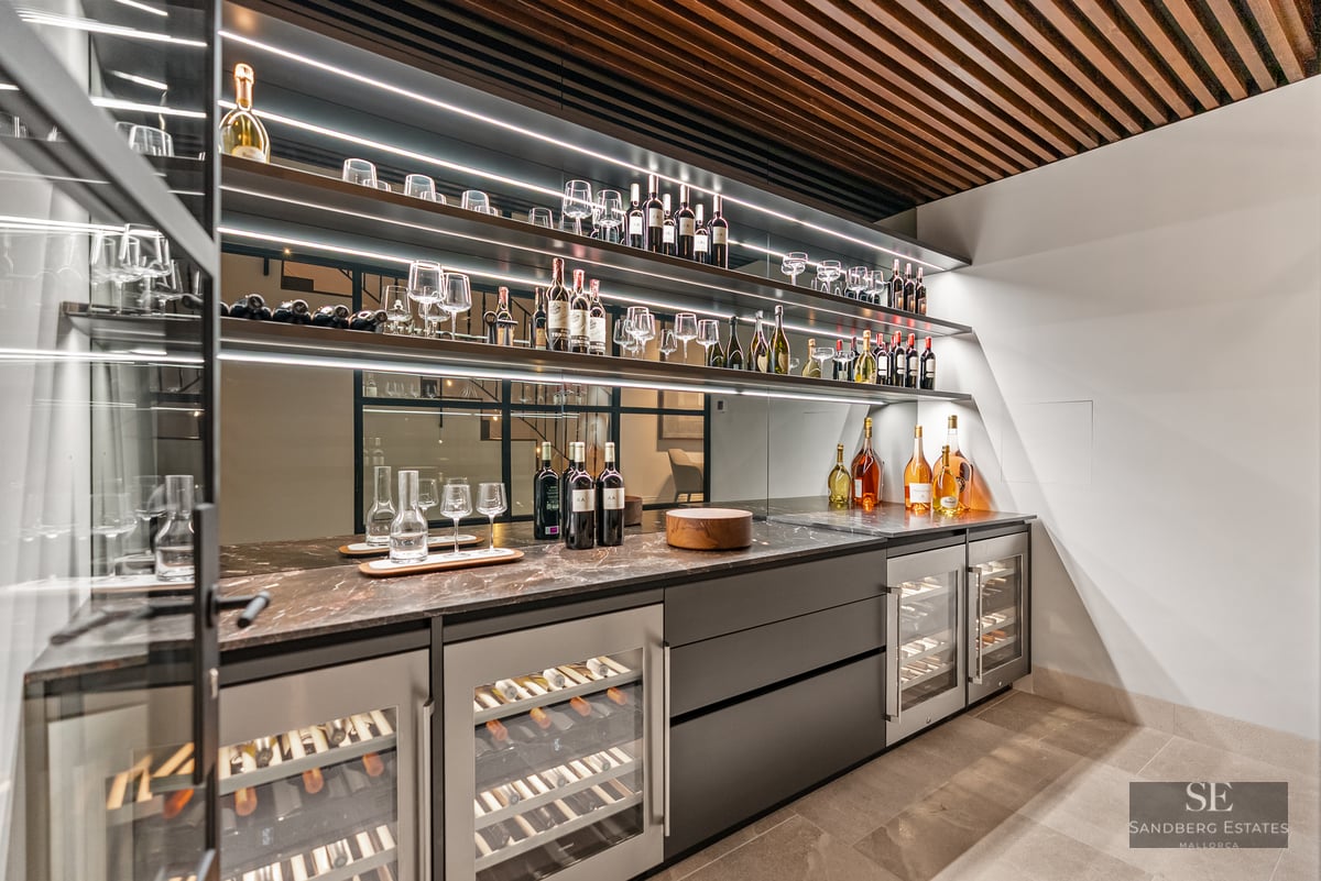 Modern wine cellar with illuminated shelves, wine coolers, marble counters, and a wooden slatted ceiling.
