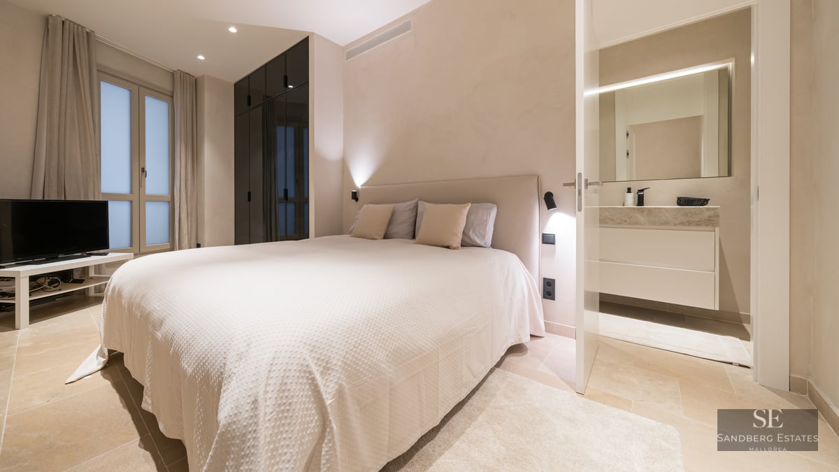 A contemporary bedroom featuring a large bed, dark glass wardrobes, and an open door leading to a modern bathroom.