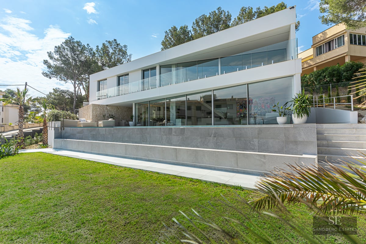 White modern villa with large windows, infinity pool, and green lawn under a sunny sky.