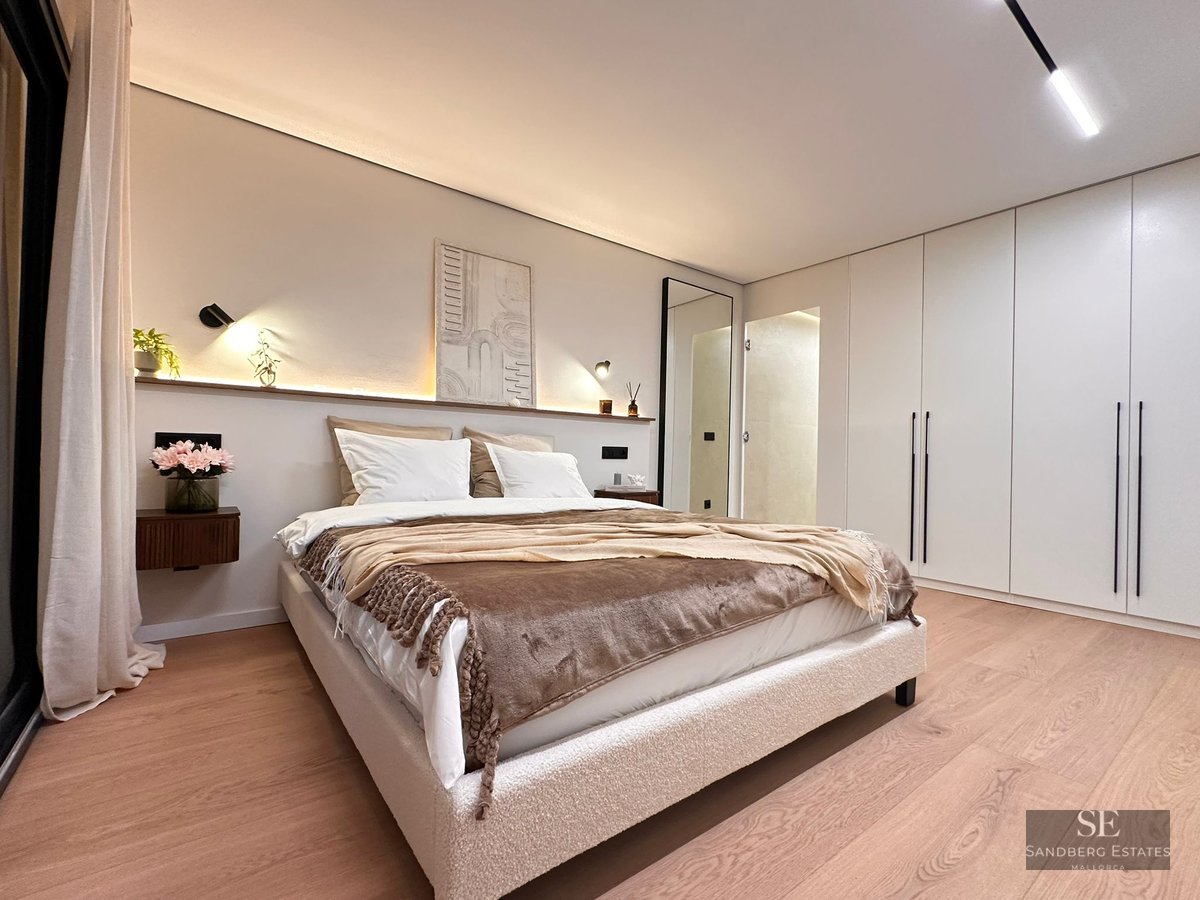 Modern master bedroom featuring a bouclé bed, ambient headboard lighting, light wood floors, and white built-in wardrobes.