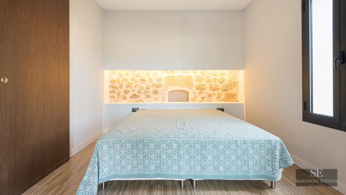 Modern bedroom featuring a bed, an illuminated natural stone wall niche, and light wood flooring.