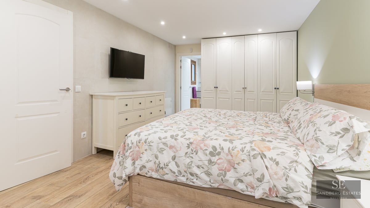 Contemporary bedroom with floral bedding, white dresser, wall-mounted TV, and large floor-to-ceiling wardrobes.