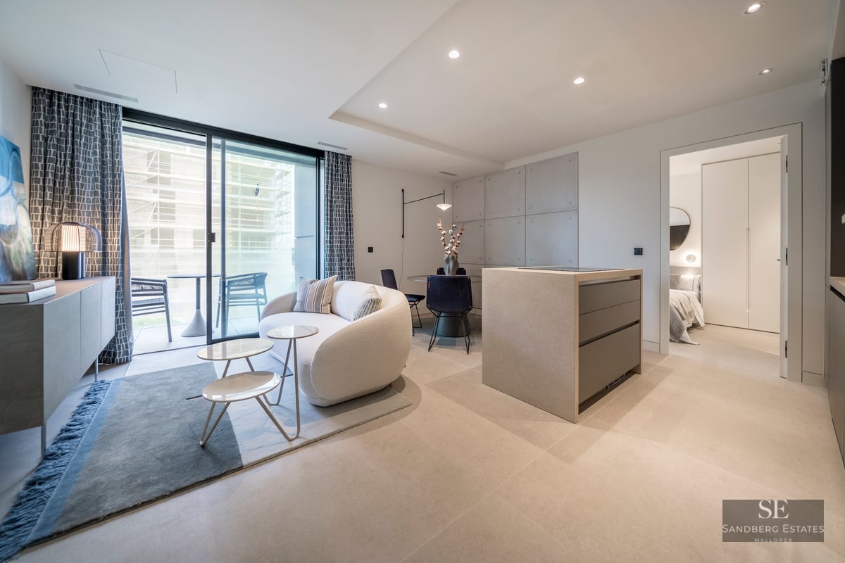 Modern living room with a white curved sofa, stone kitchen island, and large glass doors opening to a terrace.