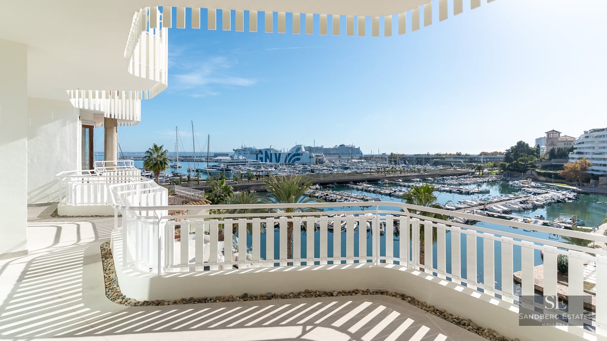 White curved balcony with modern railing overlooking a sunny marina with yachts and palm trees.