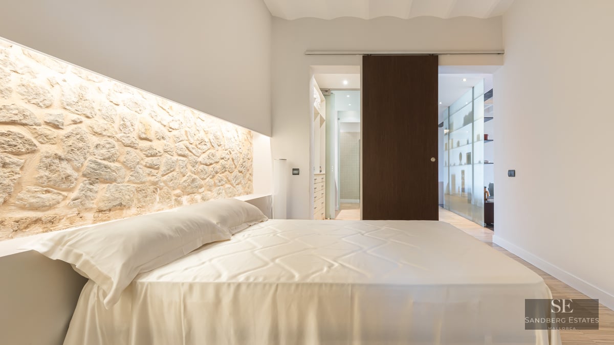 Luxury bedroom featuring a large bed, an illuminated natural stone headboard wall, and a dark wood sliding door.
