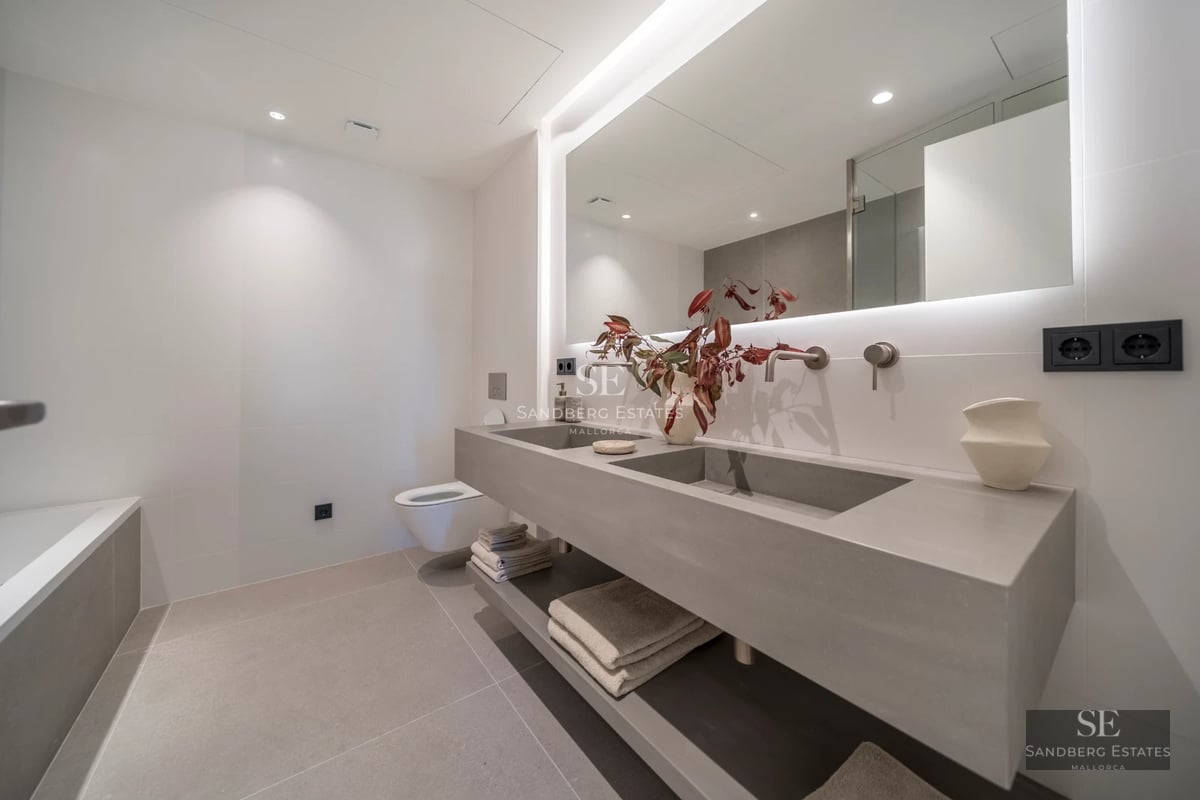 Infinity pool with sea view, surrounded by light-colored tiles and lush vegetation. Modern and elegant design.