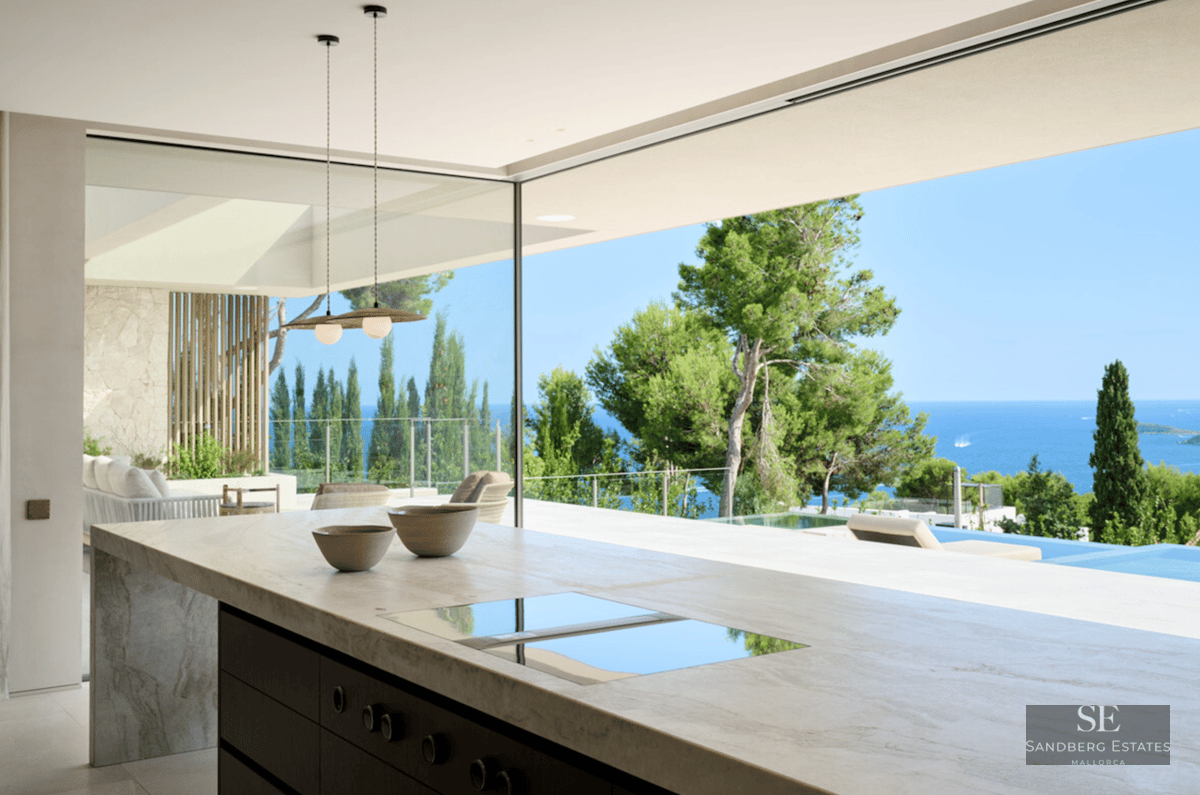 Luxury marble kitchen island facing a large open glass wall with views of a pool and the blue Mediterranean sea.