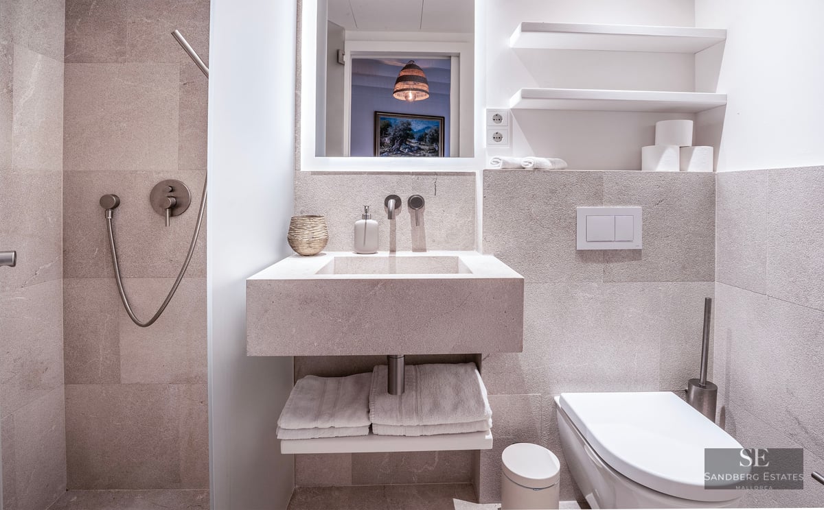 Salle de bain minimaliste avec murs en pierre, lavabo intégré, toilettes suspendues et douche à main chromée.
