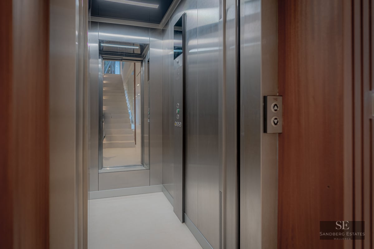 Interior of a modern elevator with stainless steel finishes, wood paneling, and a mirror reflecting a staircase.