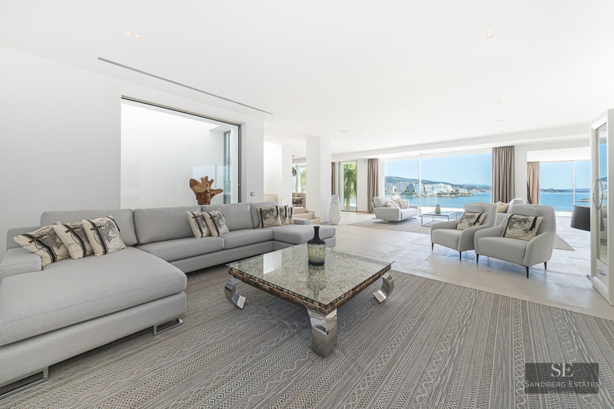 Spacious modern living room with light gray sofas, a glass coffee table, and large windows overlooking the Mediterranean sea.