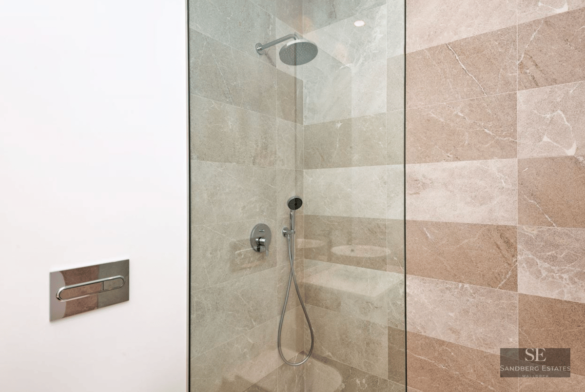 Walk-in shower with rain head, glass screen, and beige stone wall tiles.