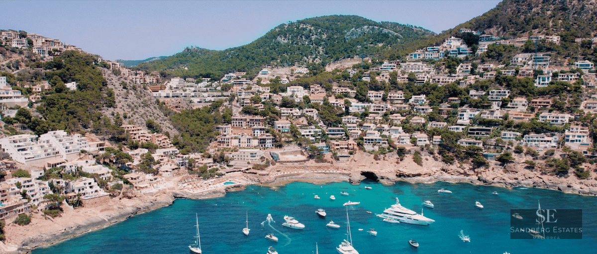 High-angle view of white houses on a green hillside overlooking a bay with many yachts and turquoise water.