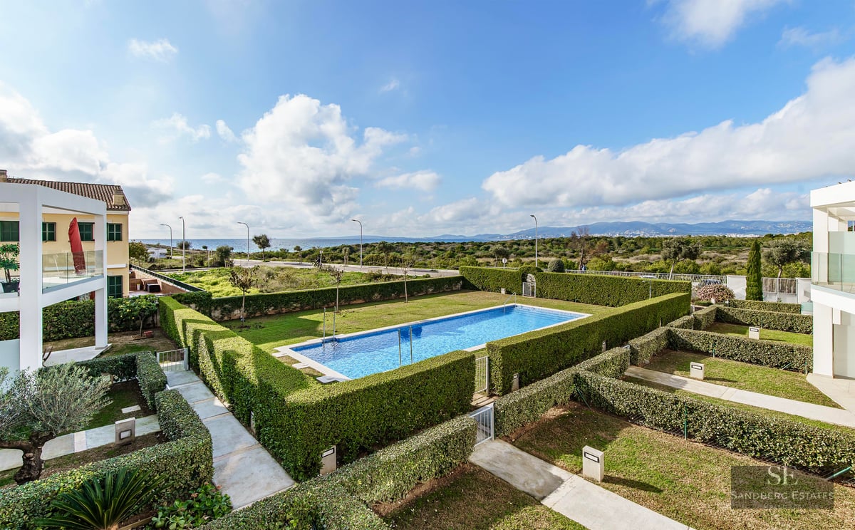 Rectangular blue swimming pool surrounded by manicured green hedges with a view of the sea in the distance.