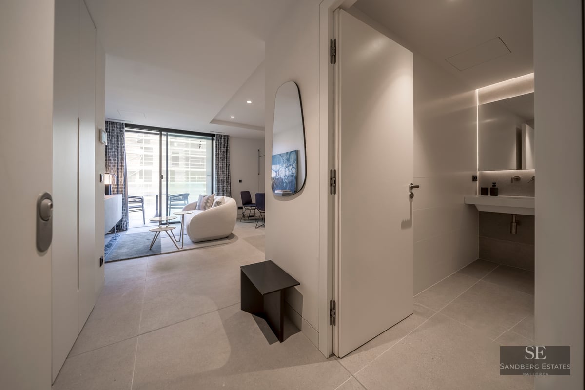 Modern hallway leading to a bright living room with a curved sofa and a sleek bathroom on the right.