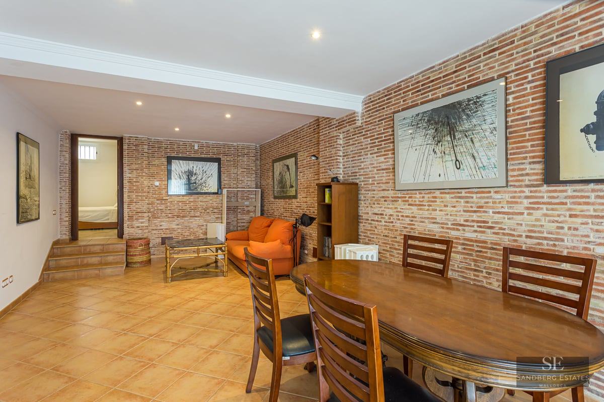 Interior view showing a wooden dining table and an orange sofa against an exposed brick wall.
