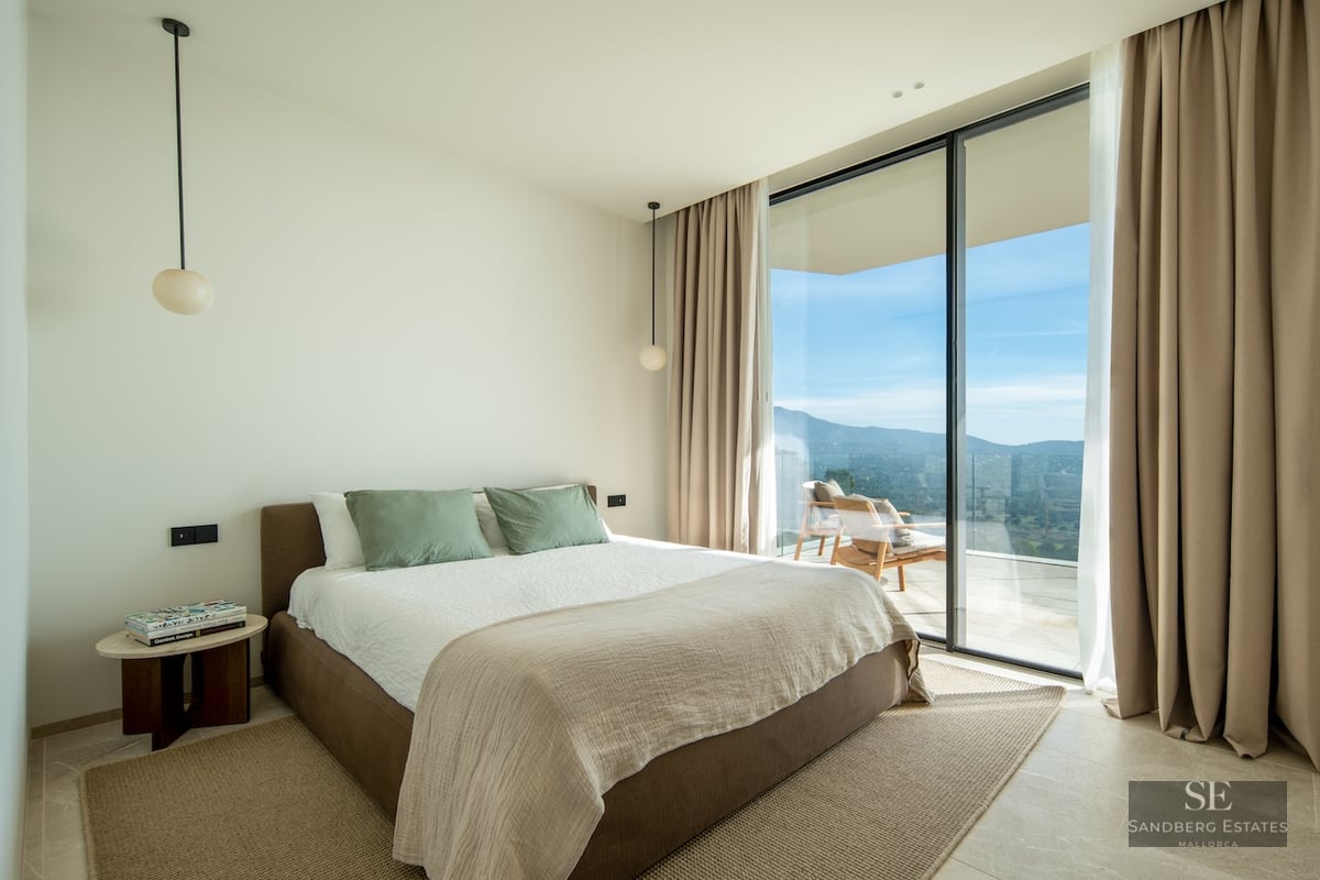 Modern bedroom with floor-to-ceiling windows leading to a terrace overlooking mountains.