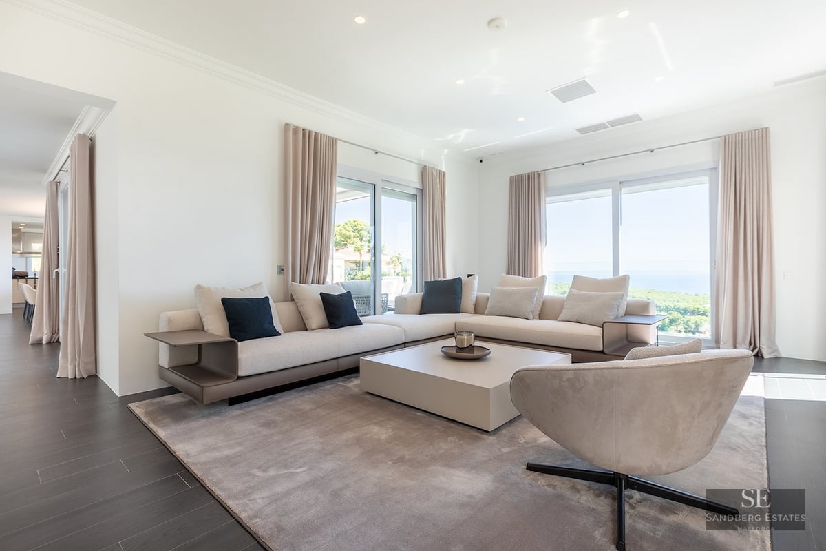 Spacious white living room with beige sectional sofa, designer armchair, and large windows overlooking the ocean.