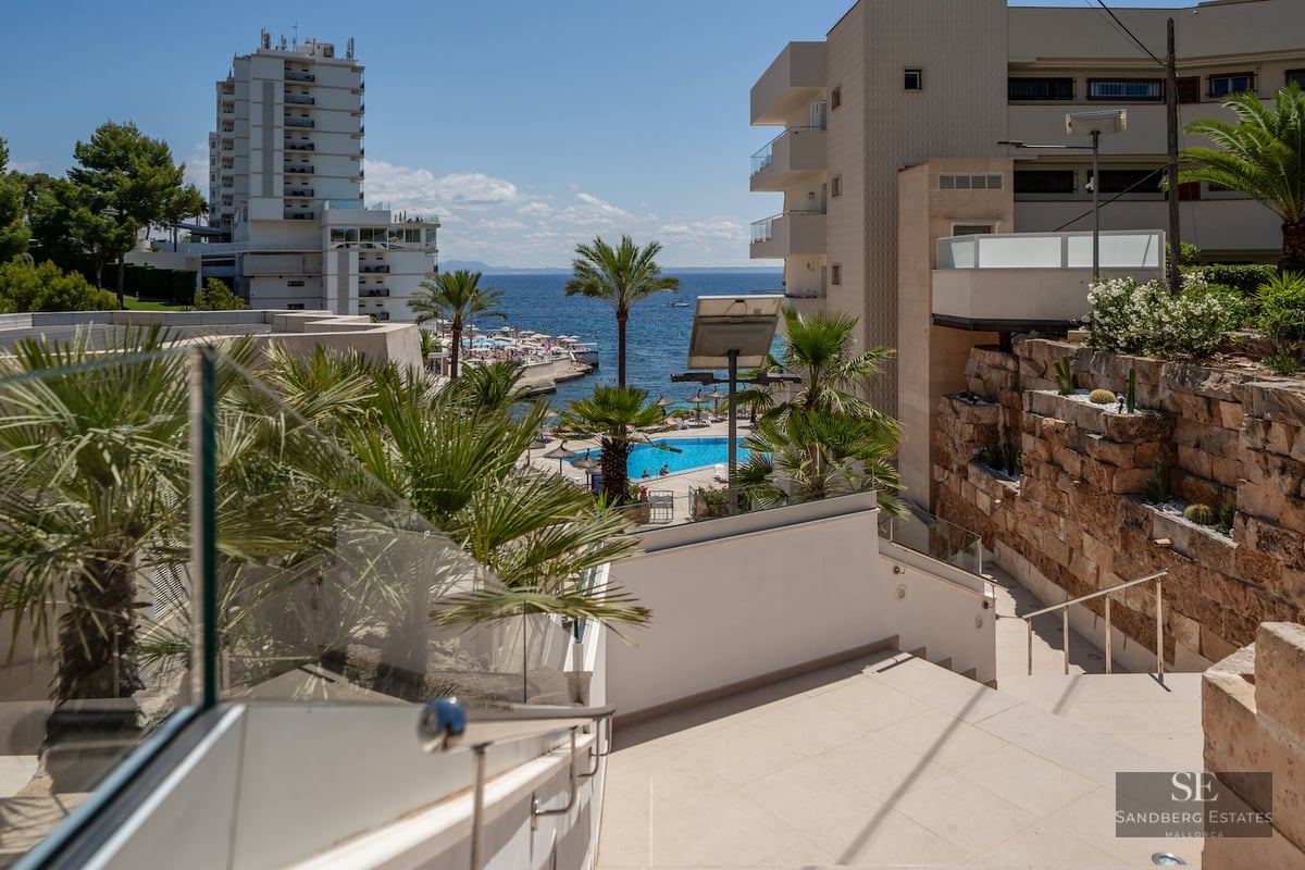 Outdoor stairs with glass railings looking out over a resort pool and the blue Mediterranean Sea.