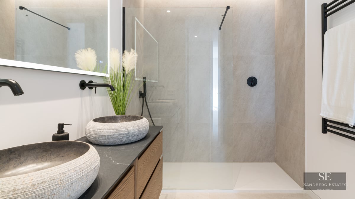 Modern bathroom featuring textured stone bowl sinks, matte black fixtures, and a spacious glass shower enclosure.