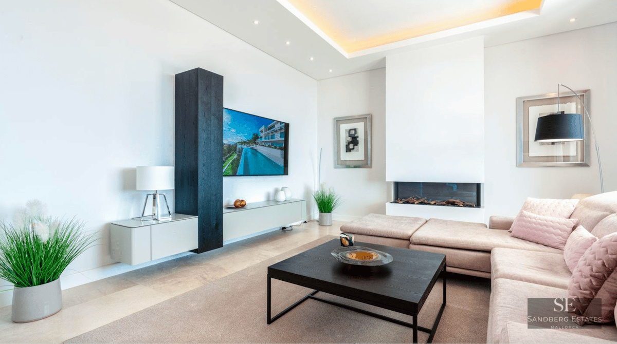 Bright living room featuring a beige sofa, black coffee table, wall-mounted TV, and modern inset fireplace.