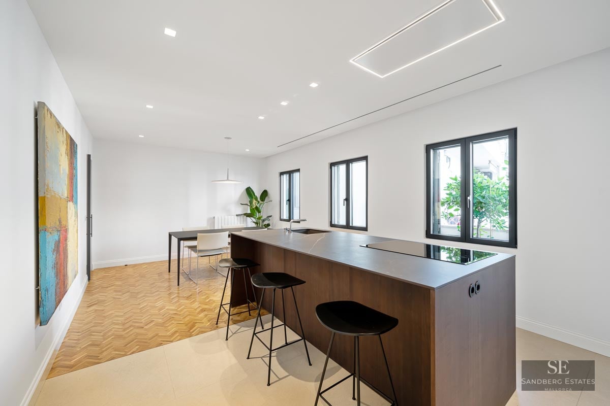 Minimalist kitchen featuring a dark wood island, black bar stools, herringbone wood flooring, and abstract wall art.