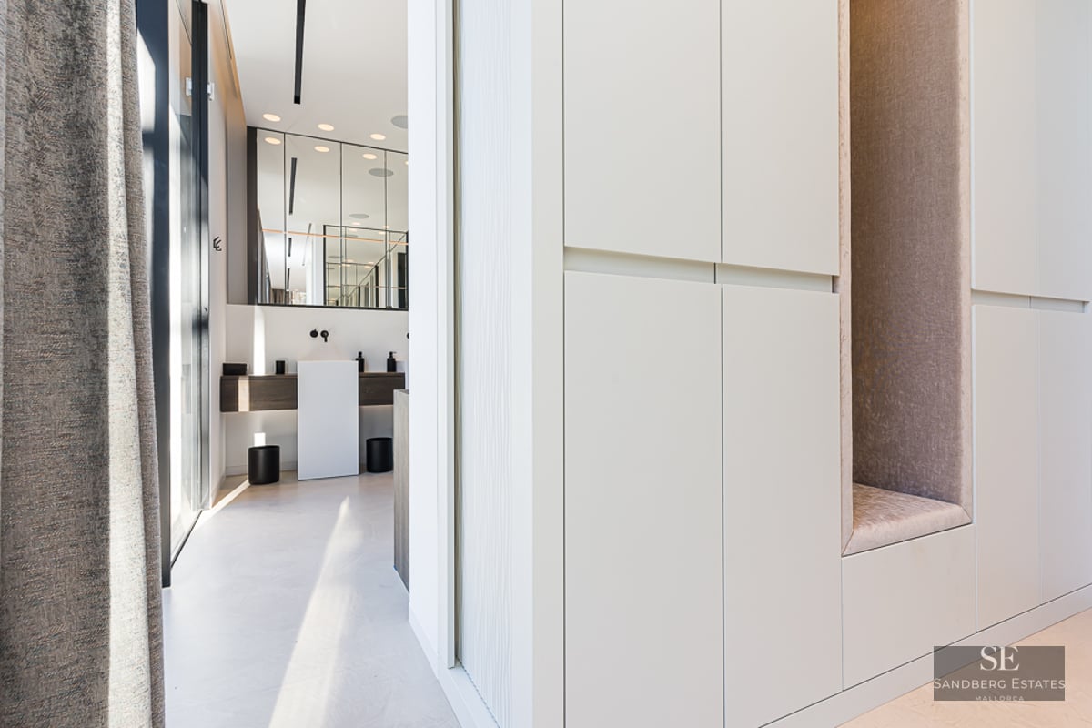 White built-in closets with a cushioned niche leading to a modern bathroom with a pedestal sink.
