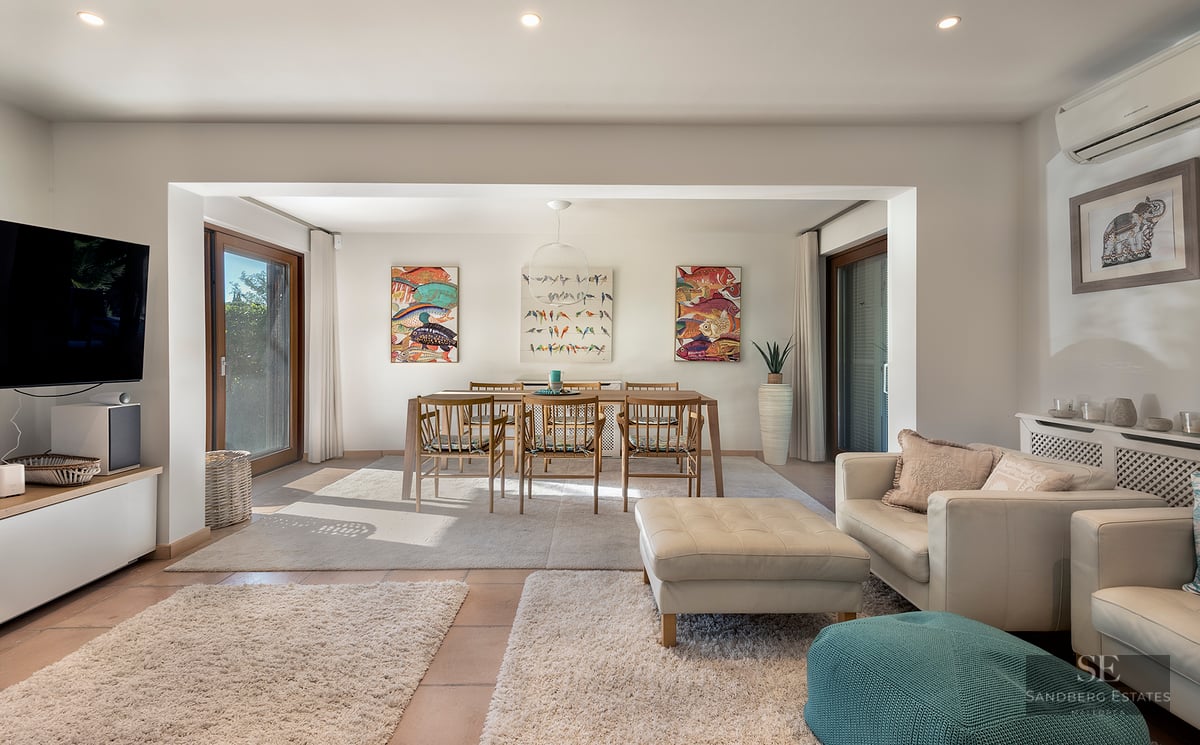 Bright open-plan living room with cream leather sofas, wooden dining table, and colorful fish artwork on white walls.