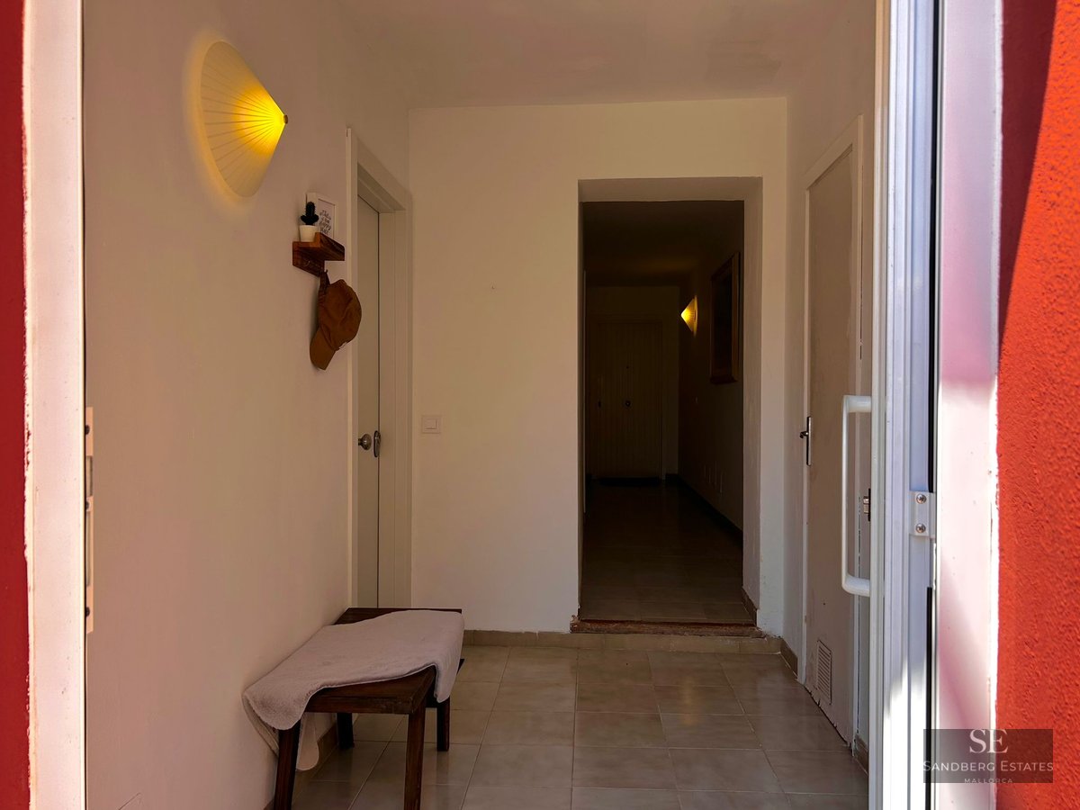 A clean white hallway with a wooden bench, tiled floor, and a glowing fan-shaped wall light near multiple white doors.