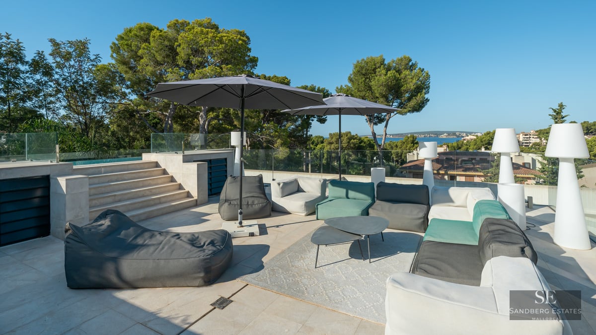 Luxurious rooftop terrace with designer lounge seating, large umbrellas, and glass railing overlooking the sea.