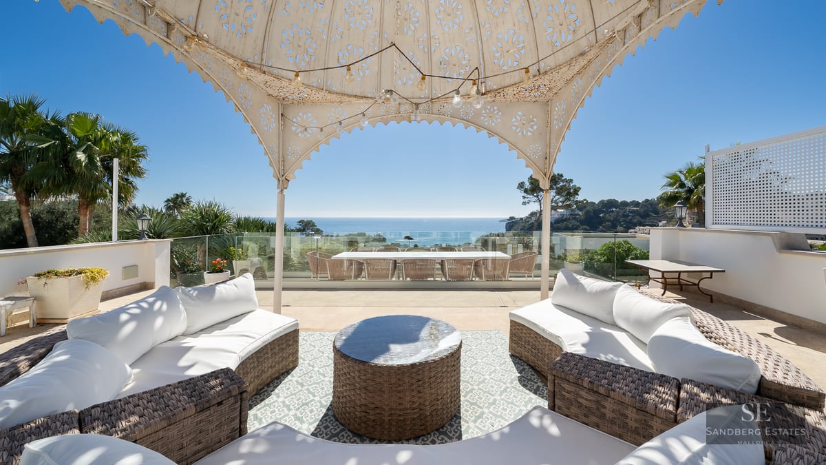 Spacious terrace with wicker sofas under a decorative gazebo overlooking the Mediterranean sea.