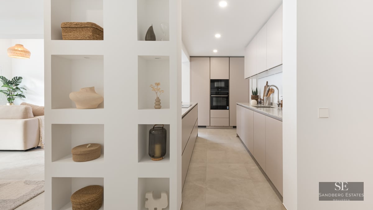 Modern galley kitchen with taupe cabinets next to a white partition wall with eight decorative recessed niches.