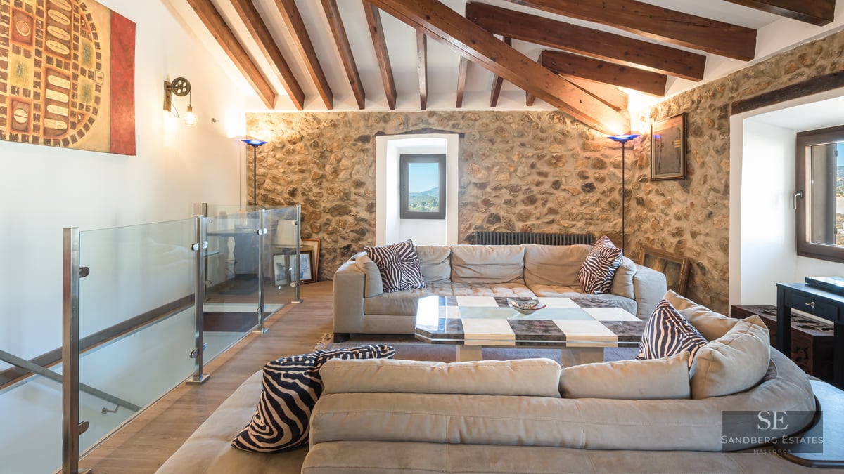 Living room featuring large sofas, exposed stone walls, wooden ceiling beams, and a glass mezzanine railing.
