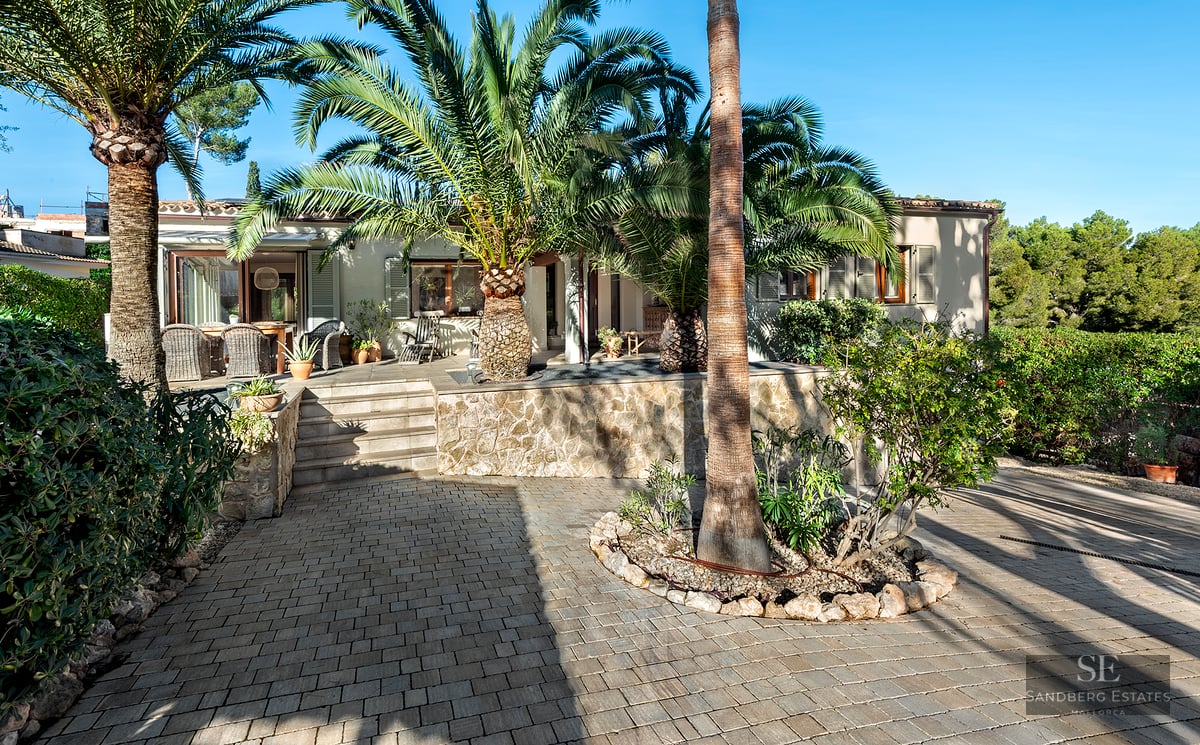 Exterior of a Mediterranean house with stone walls and large palm trees under a clear blue sky.