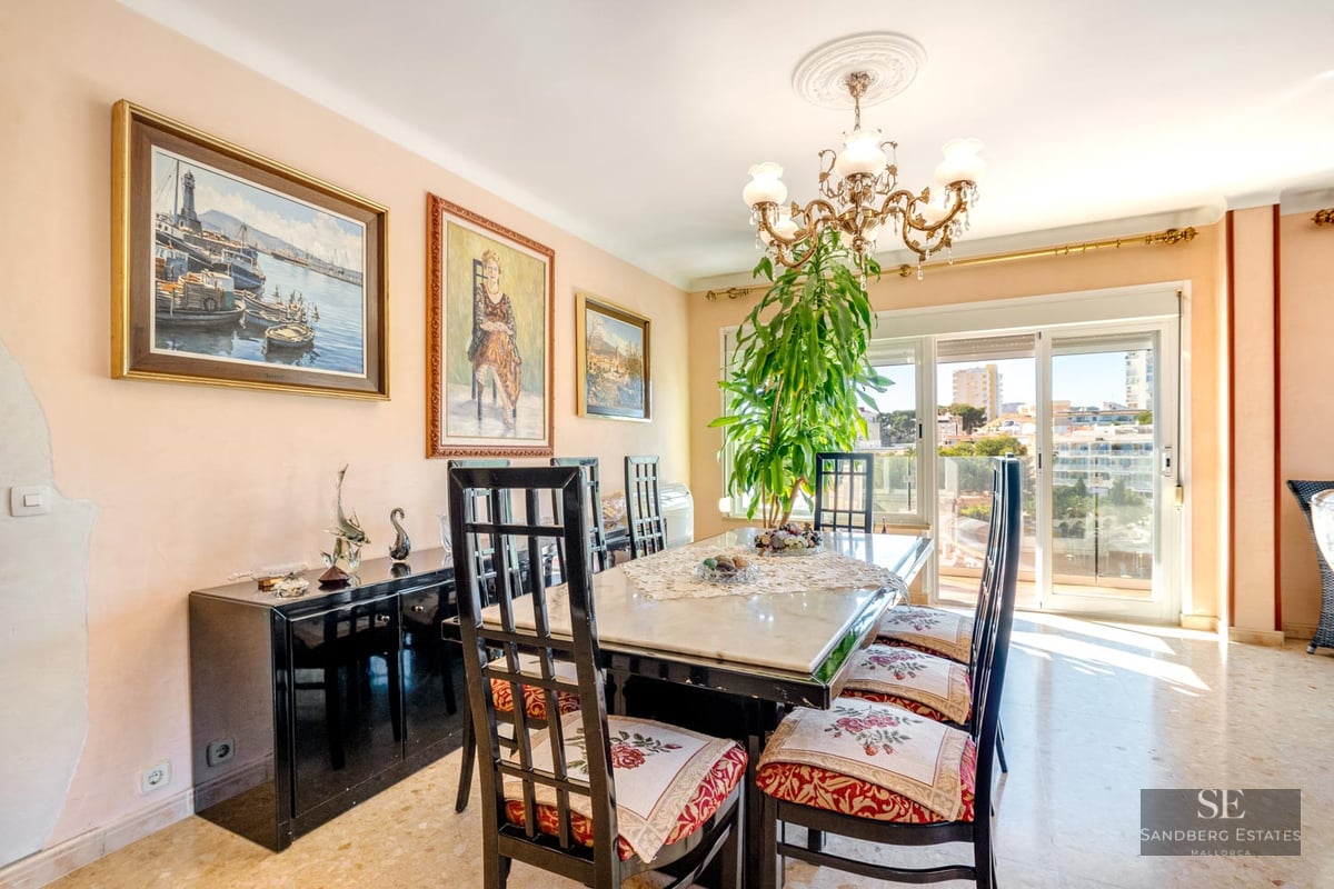 Traditional dining room with a marble table, high-backed chairs, a chandelier, and large glass doors with a city view.