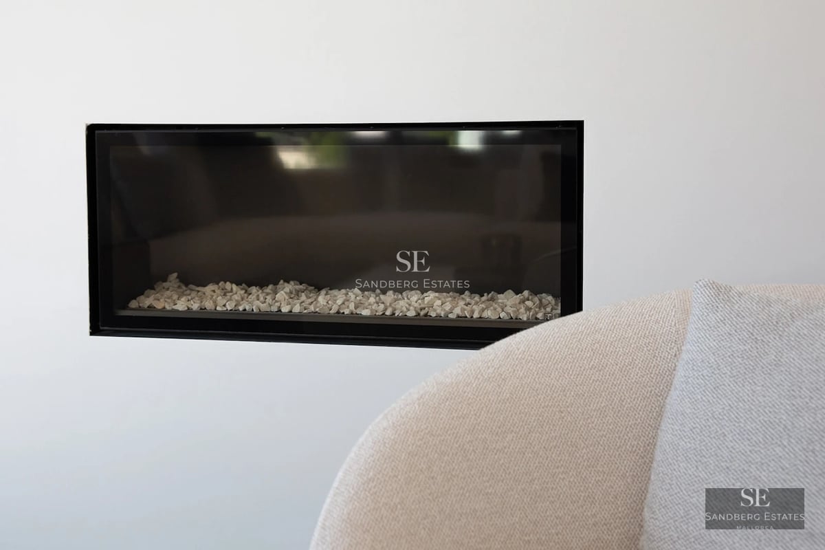 Close-up of a sleek black-framed horizontal fireplace with white stones, set into a clean white wall.