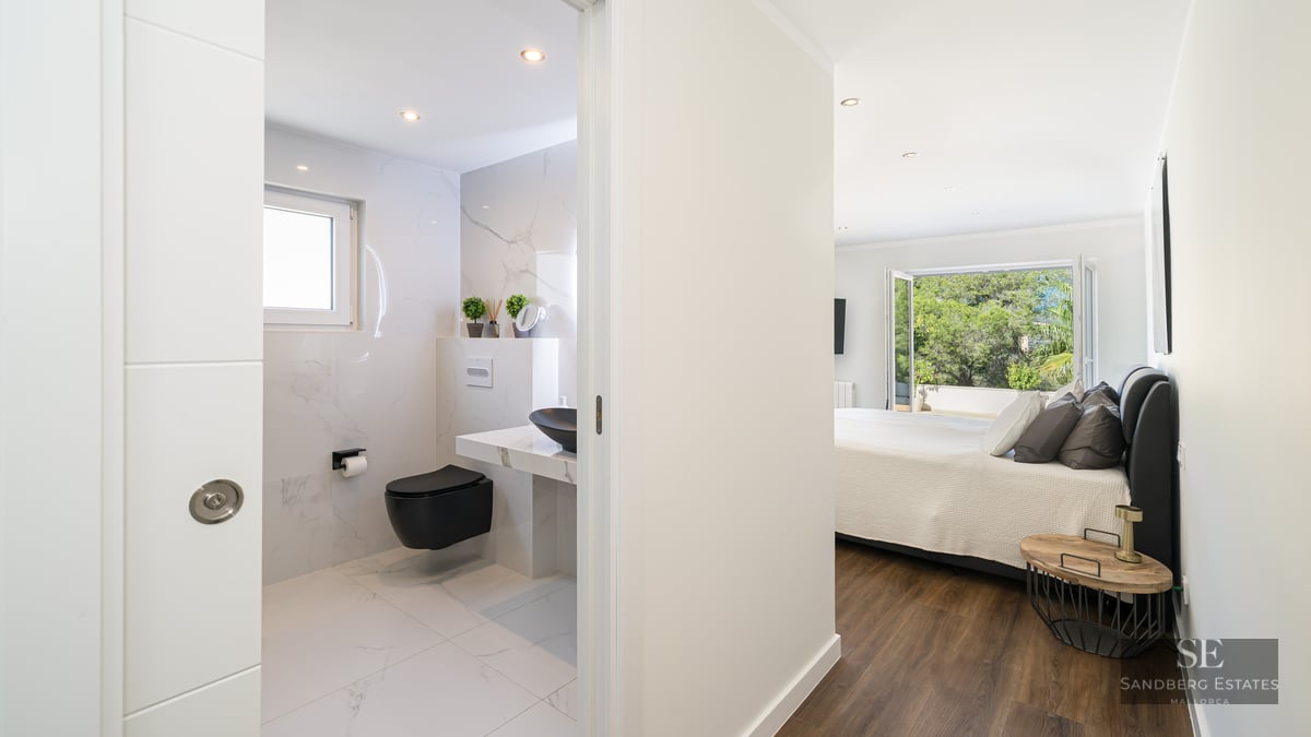 Chambre parentale lumineuse avec parquet et salle de bain moderne en marbre blanc et noir.