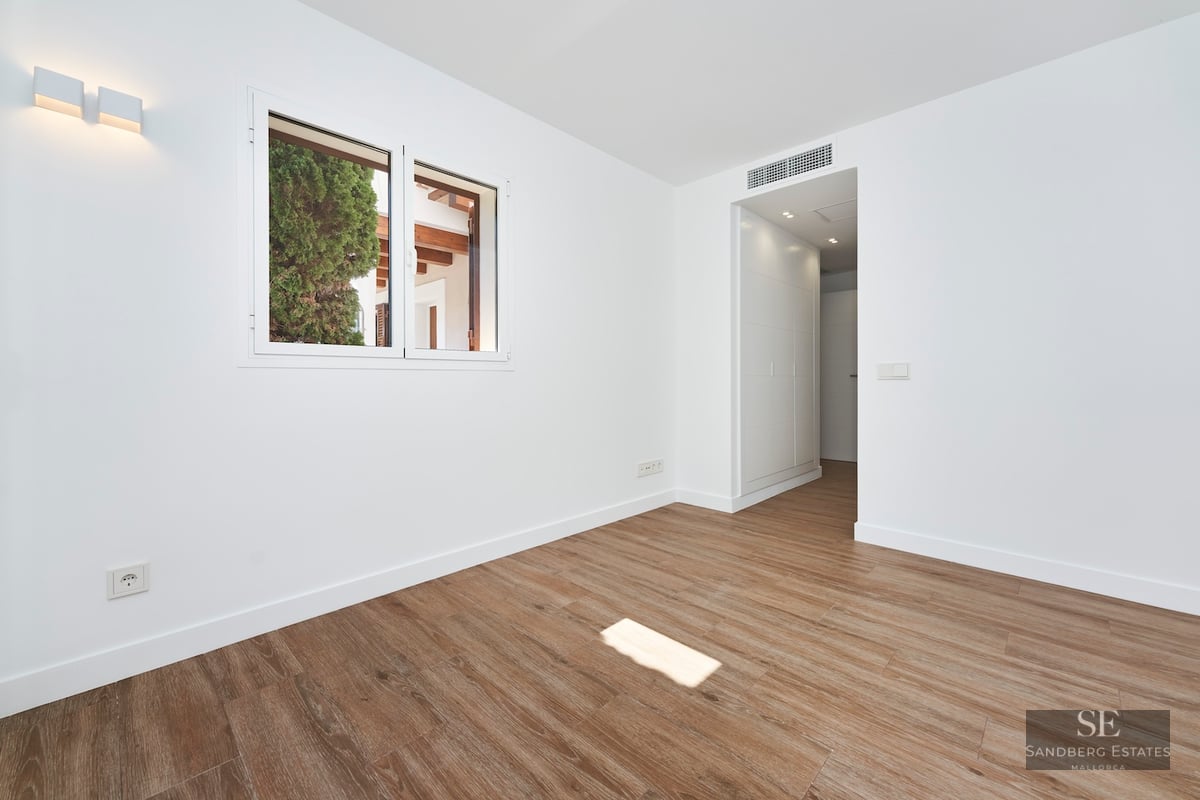 Empty room with white walls, wood-look flooring, a window, and a modern wall sconce.