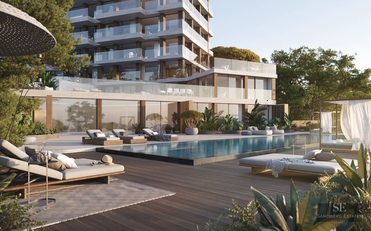Modern apartment building with a large swimming pool, wooden deck, luxury lounge chairs, and lush green gardens.