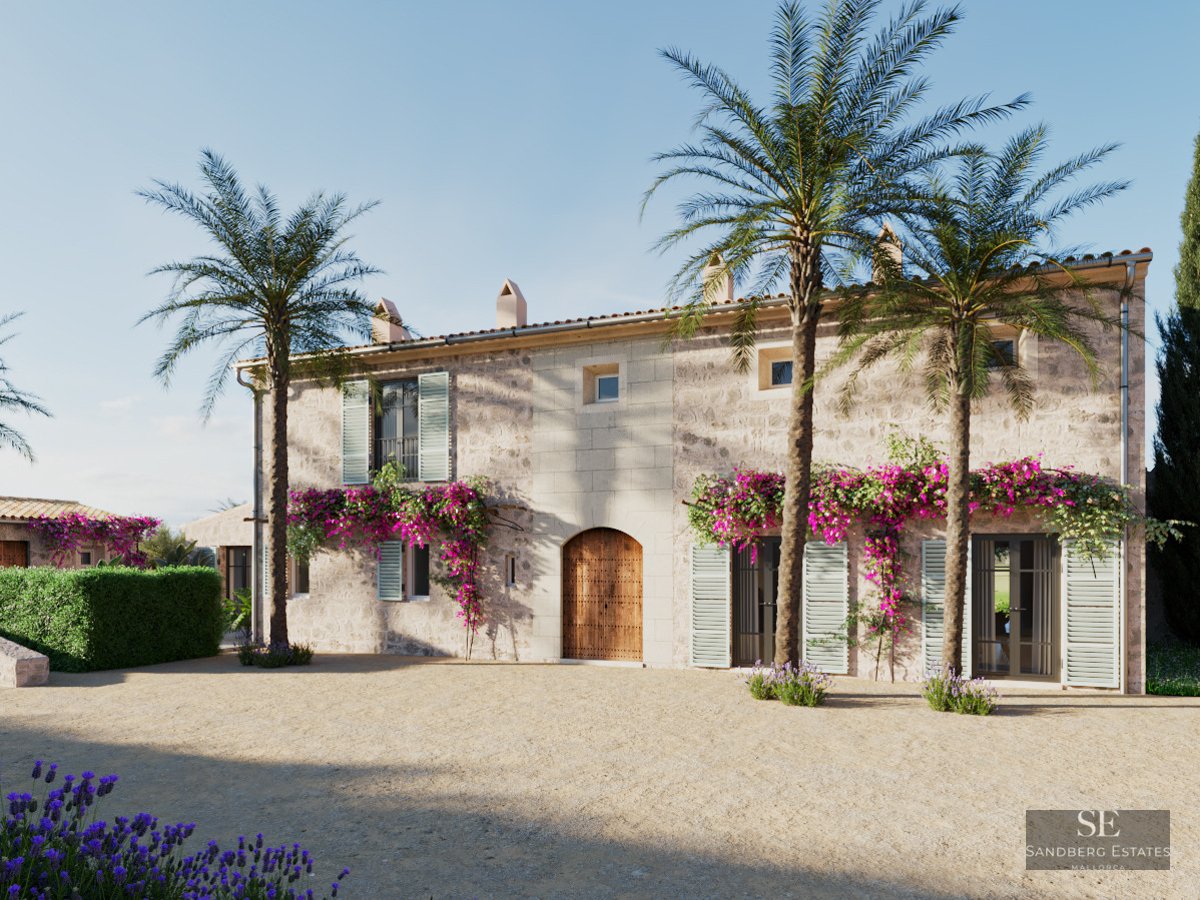Facade of a rustic stone villa with three palm trees, purple bougainvillea, and a large arched wooden door.