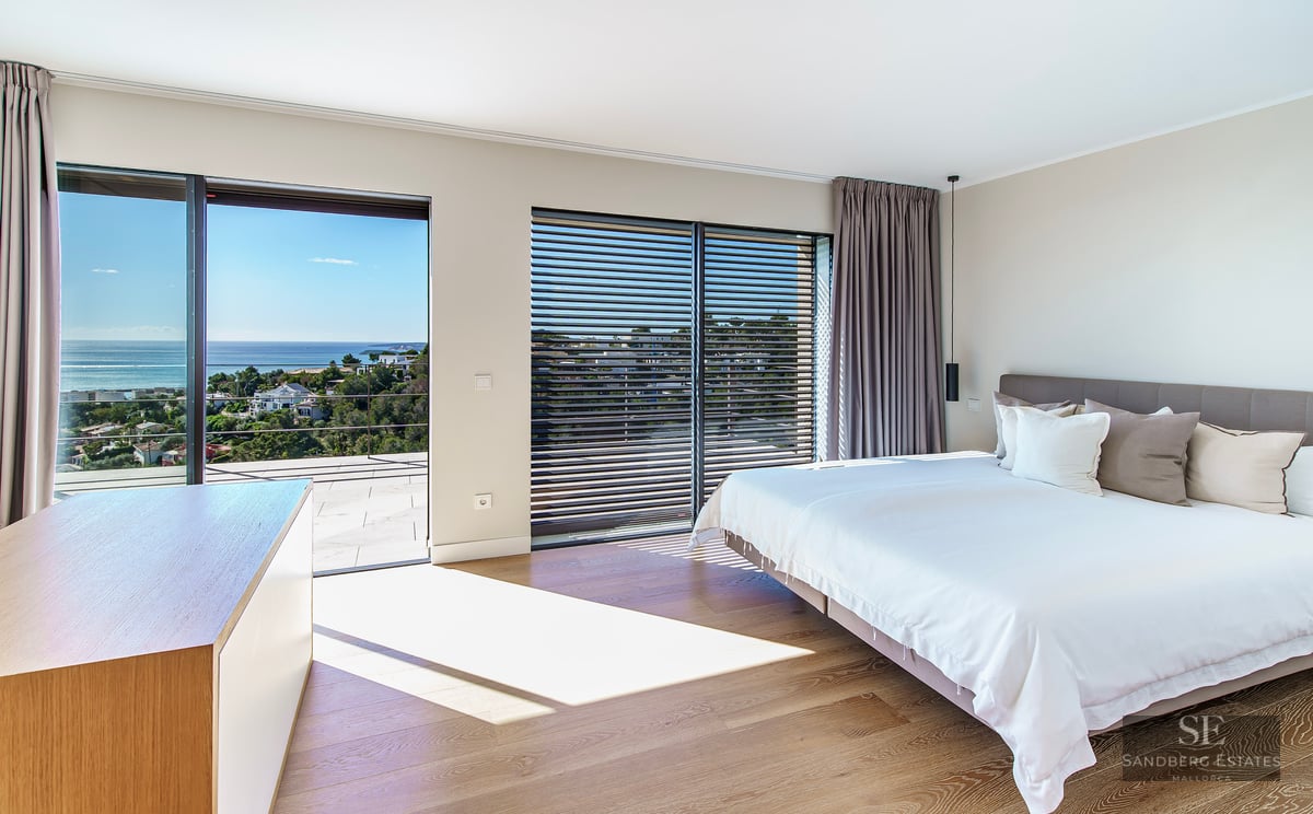 Bright modern master bedroom with large glass doors opening to a terrace overlooking the sea.