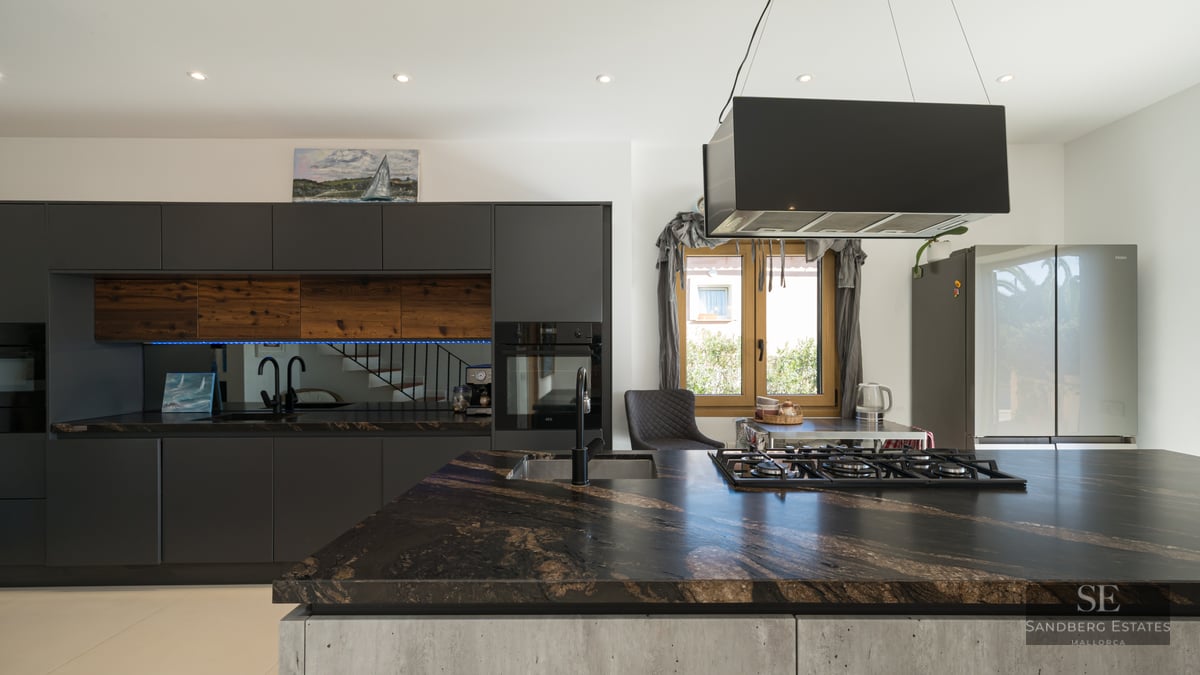 Modern kitchen with dark marble island, matte black cabinetry, and wood accents.