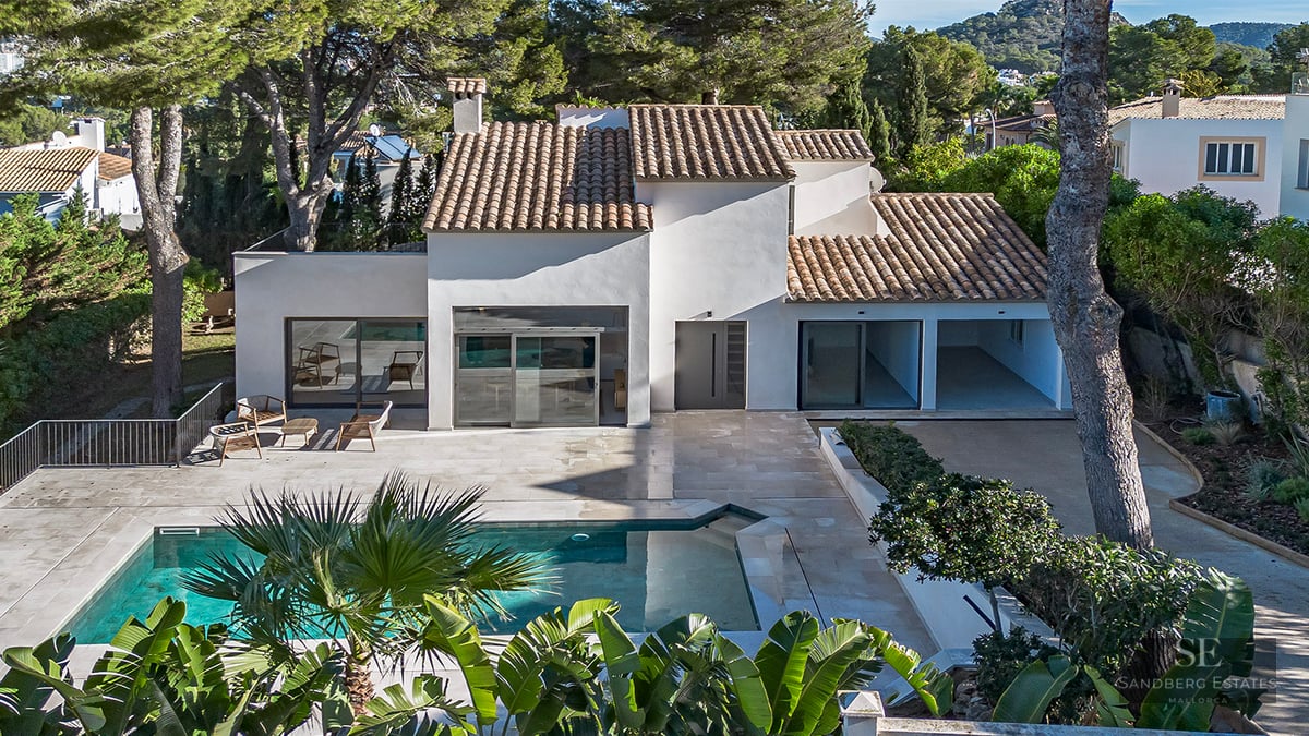 Aerial view of a white villa with a terracotta roof, a turquoise swimming pool, and stone terrace surrounded by pine trees.