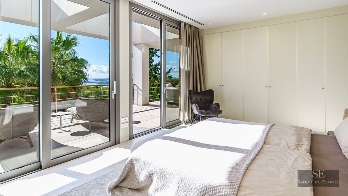 Chambre principale lumineuse avec de grandes baies vitrées ouvrant sur une terrasse ensoleillée avec vue sur la mer.