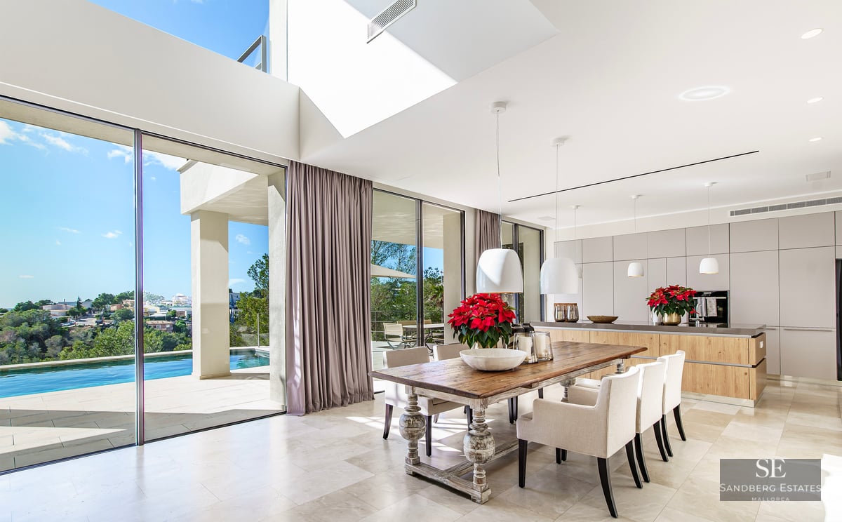 Modern open-plan dining room with a rustic wooden table and glass walls overlooking an infinity pool and valley.