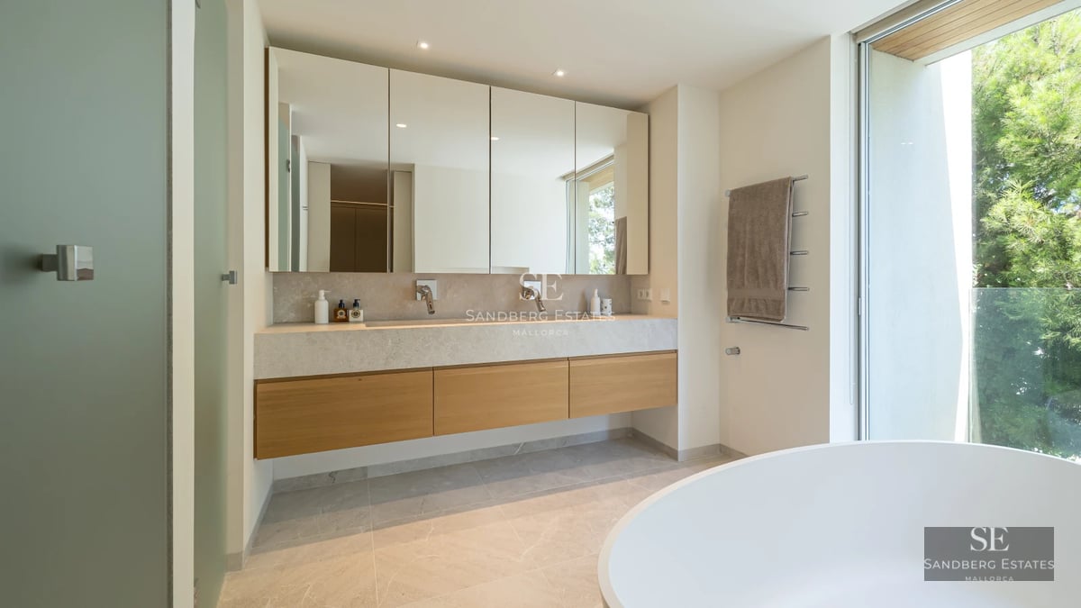 View of the pool and terrace with sun loungers, surrounded by lush greenery and modern architecture. Bright interior visible.