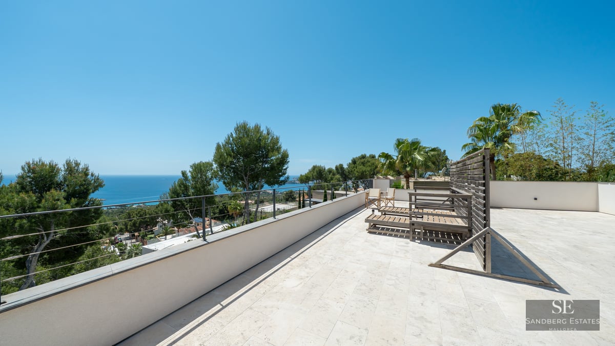 Large stone terrace with wooden loungers overlooking the Mediterranean Sea and lush trees.