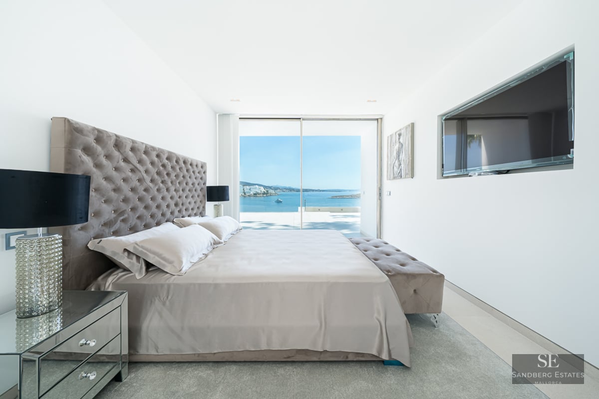 Modern master bedroom with tufted headboard, mirrored furniture, and large glass doors overlooking a blue ocean.
