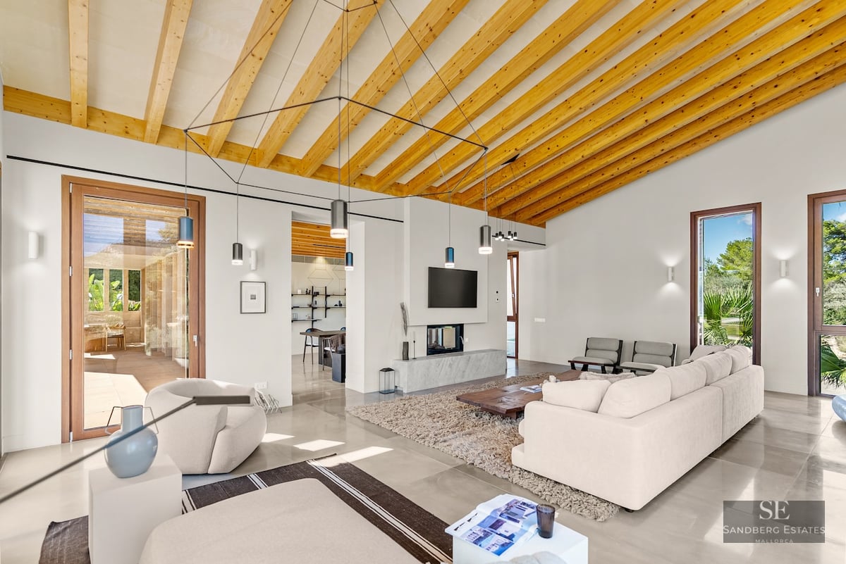 Bright living room with vaulted wood beam ceiling, cream sofas, modern fireplace, and large glass doors to a terrace.